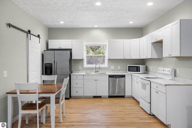 kitchen with white cabinetry, sink, a barn door, appliances with stainless steel finishes, and light wood-type flooring