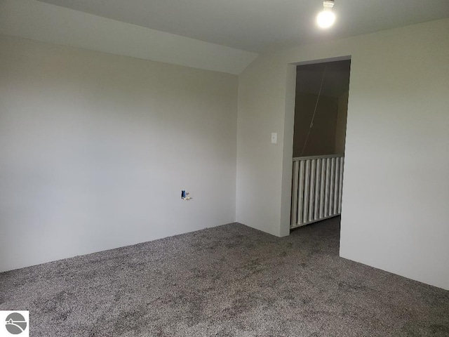 empty room featuring dark colored carpet and lofted ceiling