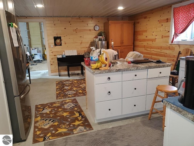 kitchen with white cabinetry, stainless steel fridge, and wooden walls