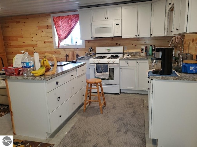 kitchen with white cabinetry, wooden walls, white appliances, and a kitchen breakfast bar