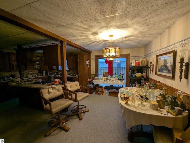 dining space featuring carpet, a paneled ceiling, and an inviting chandelier