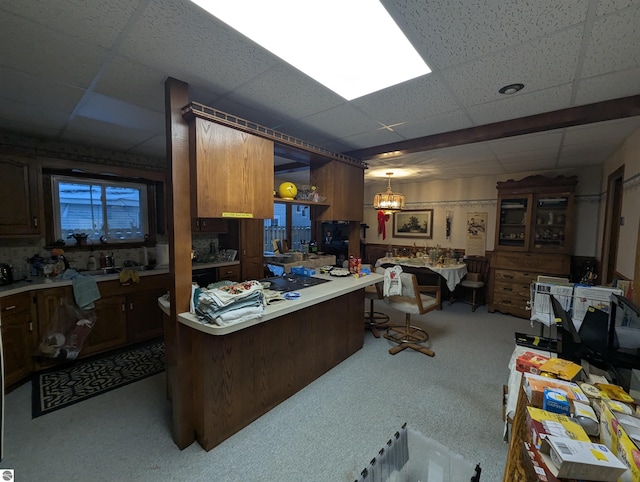 kitchen featuring a paneled ceiling, pendant lighting, light colored carpet, and kitchen peninsula