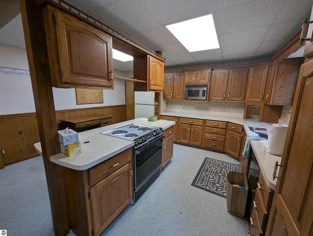 kitchen with a drop ceiling, wood walls, black range with electric stovetop, tasteful backsplash, and white fridge