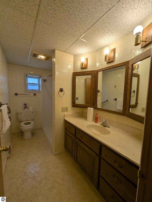 bathroom with a drop ceiling, vanity, concrete flooring, and walk in shower