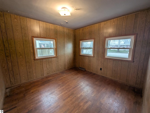 empty room featuring wooden walls, dark hardwood / wood-style floors, and a wealth of natural light