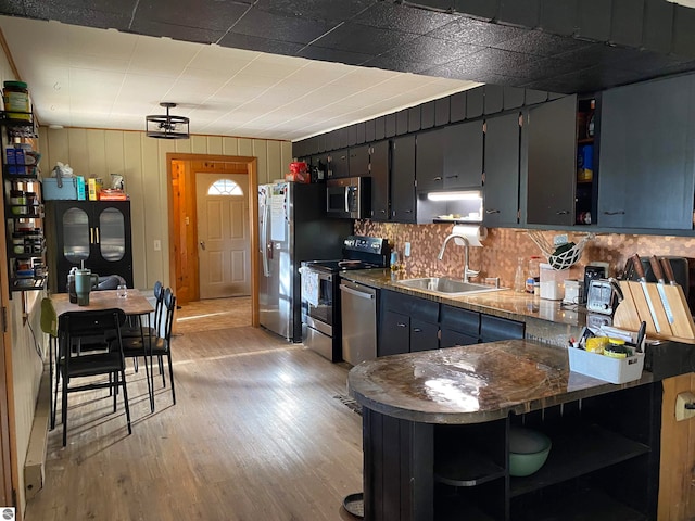 kitchen featuring wood walls, sink, light wood-type flooring, kitchen peninsula, and stainless steel appliances