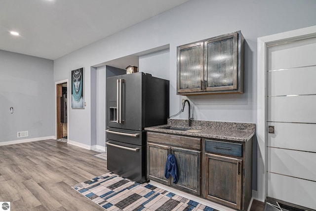 kitchen with high quality fridge, dark stone counters, dark brown cabinetry, sink, and light hardwood / wood-style flooring