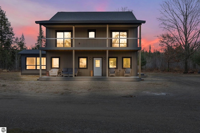 back house at dusk featuring a balcony and a porch