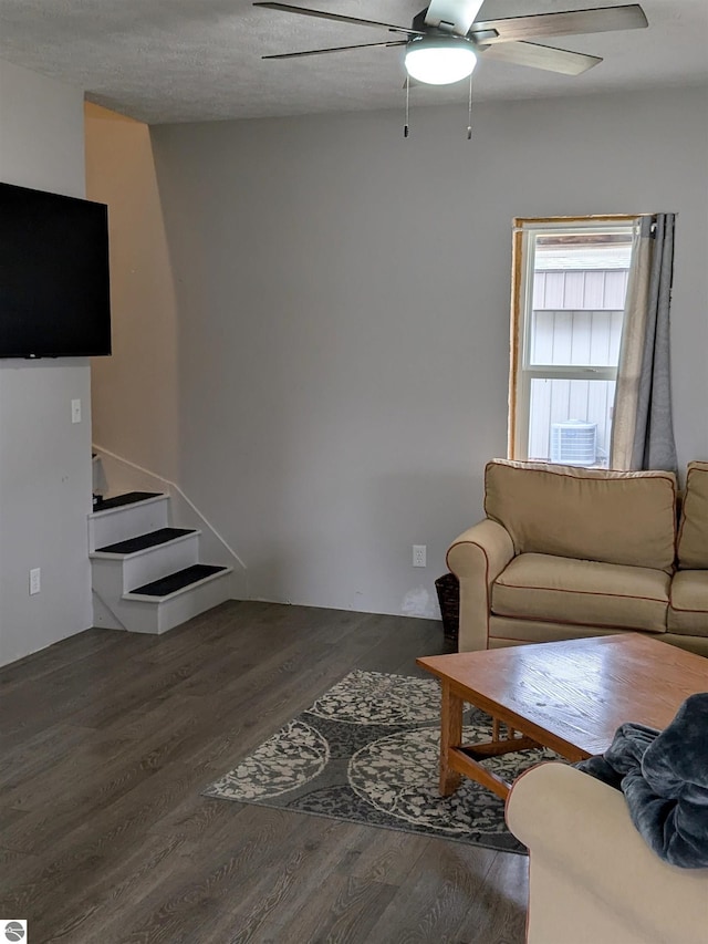 living room featuring a textured ceiling, ceiling fan, and dark wood-type flooring