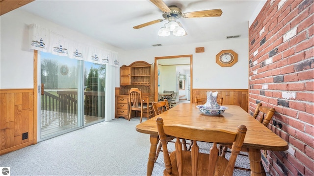 dining area featuring light colored carpet, ceiling fan, and wood walls