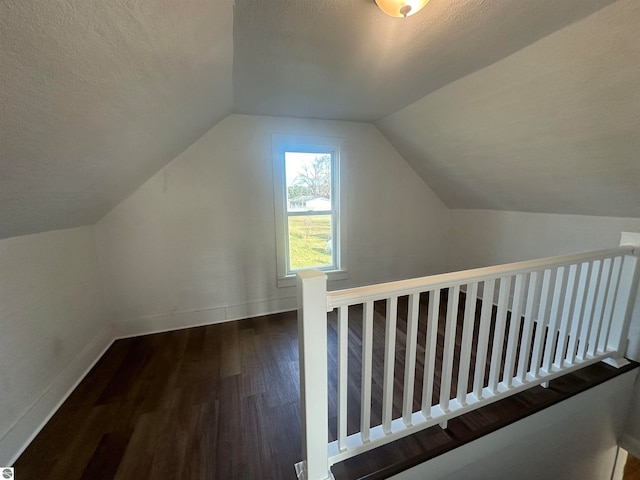 additional living space featuring a textured ceiling, dark wood-type flooring, and vaulted ceiling