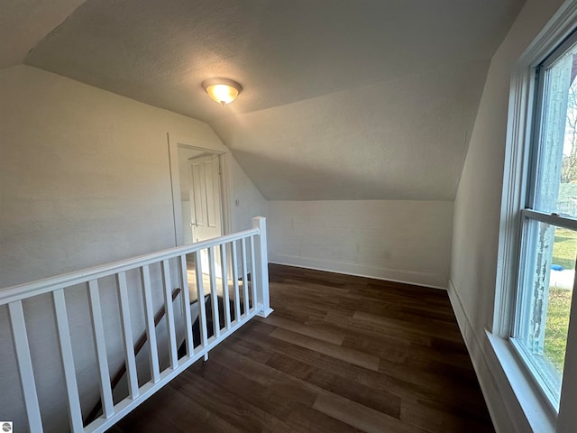 additional living space with plenty of natural light, dark hardwood / wood-style flooring, a textured ceiling, and vaulted ceiling