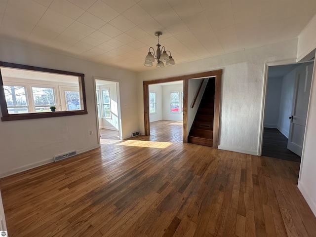 unfurnished room featuring a healthy amount of sunlight, dark wood-type flooring, and a notable chandelier