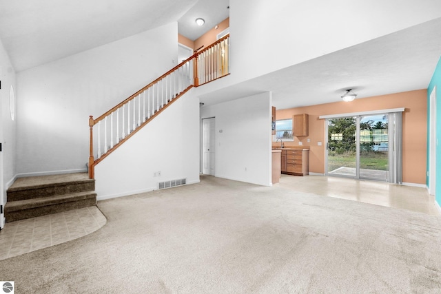 unfurnished living room with light carpet, sink, and a high ceiling