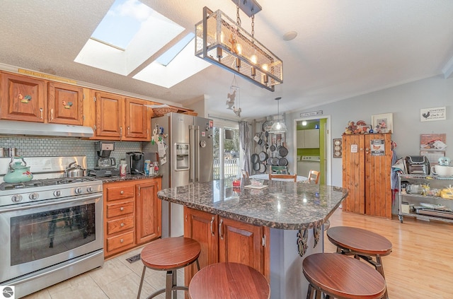 kitchen featuring a skylight, hanging light fixtures, stainless steel range with gas cooktop, a breakfast bar, and a kitchen island