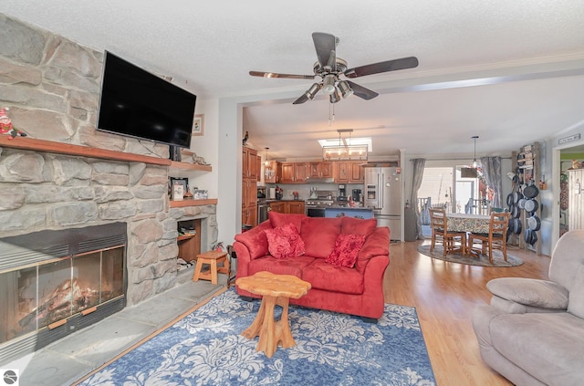 living room featuring ceiling fan, a fireplace, light hardwood / wood-style floors, and a textured ceiling