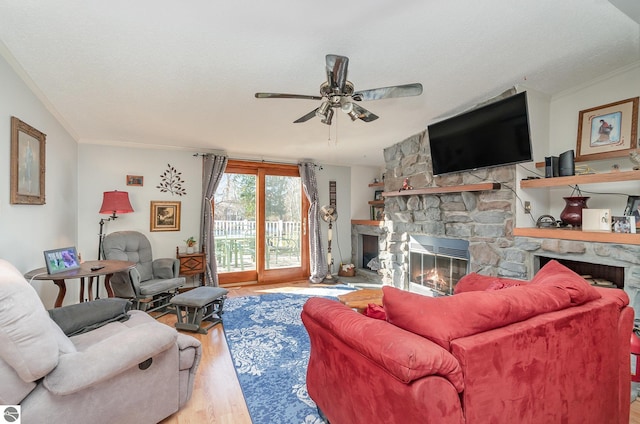 living room featuring a stone fireplace, ceiling fan, ornamental molding, and light wood-type flooring