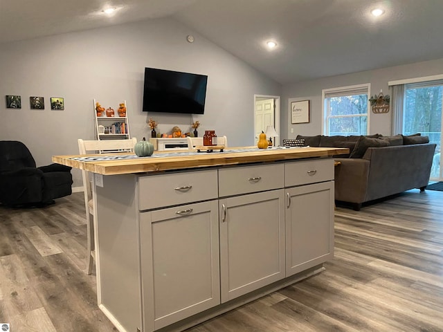 kitchen featuring butcher block countertops, a kitchen island, wood-type flooring, and lofted ceiling