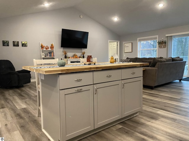 kitchen with hardwood / wood-style flooring, a kitchen island, butcher block countertops, and vaulted ceiling