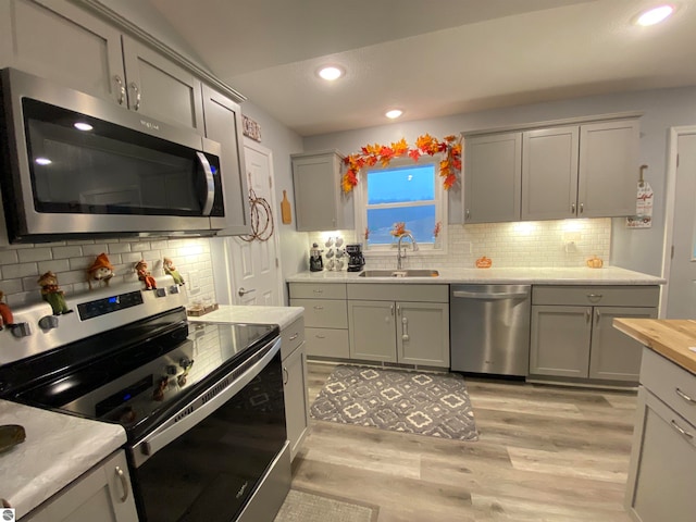 kitchen featuring light wood-type flooring, backsplash, stainless steel appliances, sink, and butcher block counters