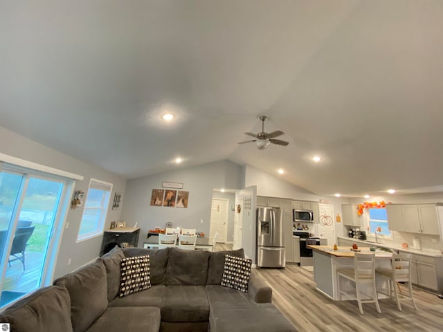 living room with ceiling fan, light hardwood / wood-style floors, and vaulted ceiling