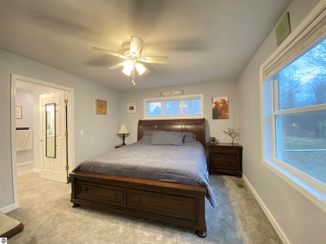 bedroom with multiple windows, ceiling fan, ensuite bath, and light colored carpet