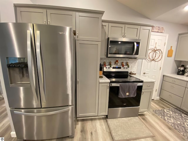 kitchen featuring gray cabinetry, backsplash, vaulted ceiling, light hardwood / wood-style flooring, and appliances with stainless steel finishes