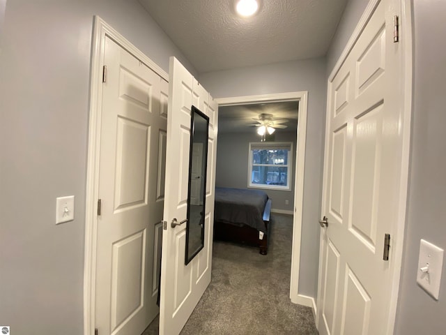 hallway featuring dark colored carpet and a textured ceiling