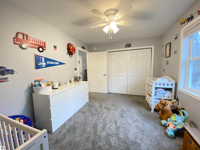 bedroom featuring dark colored carpet, ceiling fan, a crib, and a closet