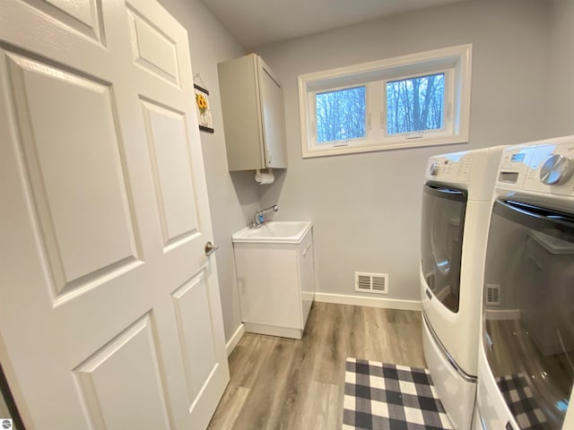 laundry room featuring cabinets, independent washer and dryer, sink, and light hardwood / wood-style flooring