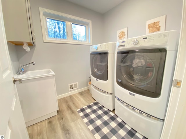 laundry area featuring washer and dryer, light hardwood / wood-style floors, cabinets, and sink