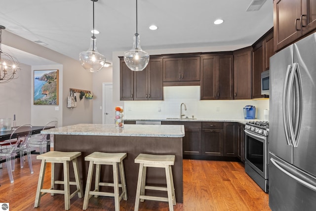 kitchen featuring light stone countertops, stainless steel appliances, decorative light fixtures, light hardwood / wood-style flooring, and a kitchen island