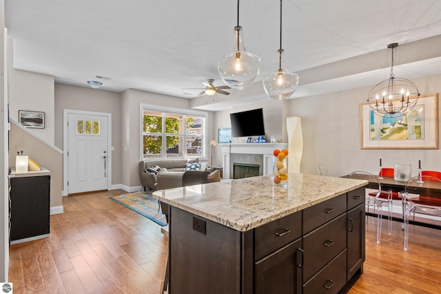 kitchen with ceiling fan with notable chandelier, dark brown cabinetry, light hardwood / wood-style flooring, a kitchen island, and hanging light fixtures