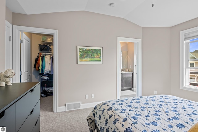 bedroom featuring ensuite bathroom, light colored carpet, lofted ceiling, a walk in closet, and a closet