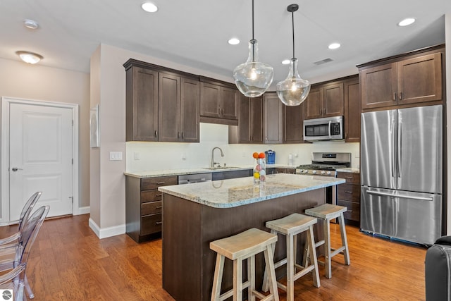 kitchen with light stone countertops, stainless steel appliances, pendant lighting, wood-type flooring, and a kitchen island