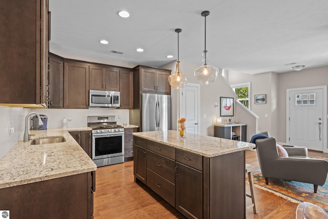 kitchen with a center island, sink, hanging light fixtures, stainless steel appliances, and light hardwood / wood-style floors