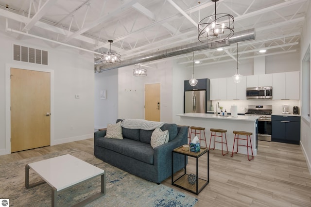 living room featuring a chandelier, a towering ceiling, light hardwood / wood-style flooring, and sink