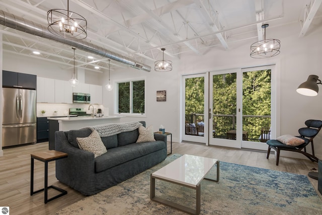 living room with light hardwood / wood-style floors, a towering ceiling, and an inviting chandelier