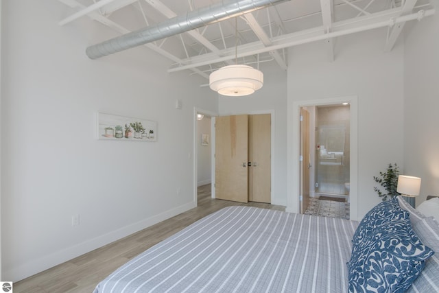 bedroom with a towering ceiling, hardwood / wood-style flooring, and ensuite bath