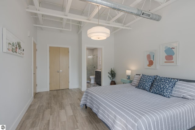 bedroom with hardwood / wood-style floors, a towering ceiling, and connected bathroom