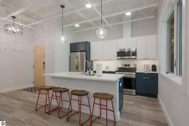 kitchen featuring hanging light fixtures, stainless steel appliances, an island with sink, a towering ceiling, and a breakfast bar