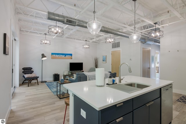 kitchen with sink, stainless steel dishwasher, decorative light fixtures, a kitchen island with sink, and light wood-type flooring