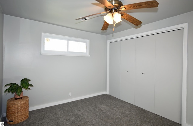 unfurnished bedroom with a closet, dark carpet, and ceiling fan