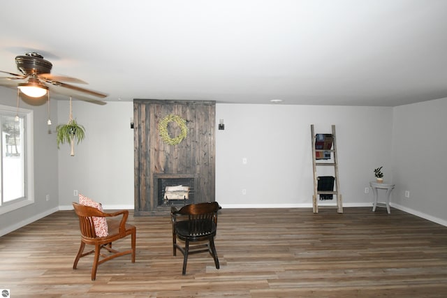 living area with hardwood / wood-style floors, ceiling fan, and a large fireplace