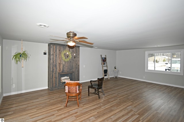 living area with ceiling fan, a large fireplace, and hardwood / wood-style flooring