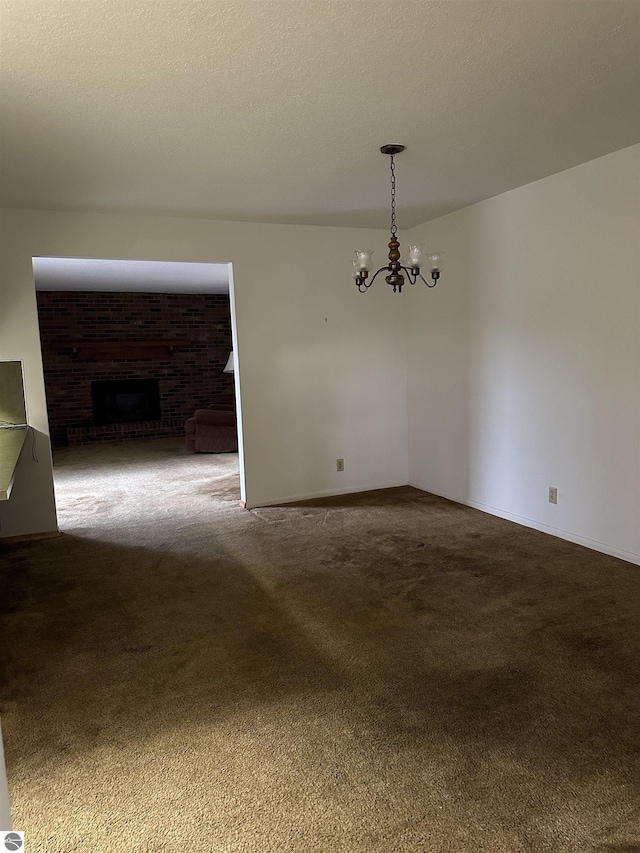 empty room featuring a fireplace, dark colored carpet, and a notable chandelier