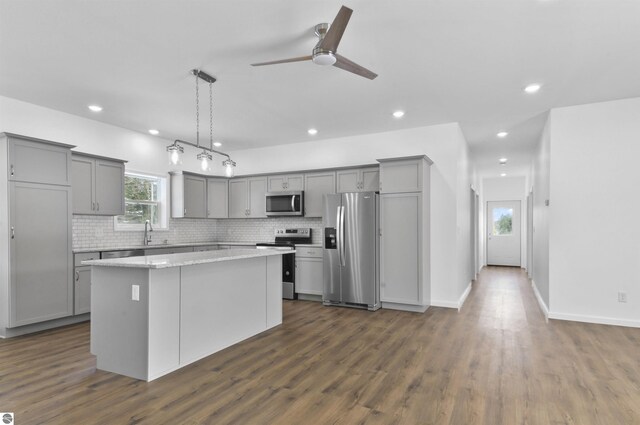 kitchen with stainless steel appliances, a kitchen island, hanging light fixtures, and dark wood-type flooring