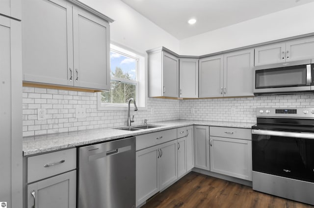 kitchen featuring appliances with stainless steel finishes, light stone counters, gray cabinetry, sink, and dark hardwood / wood-style floors