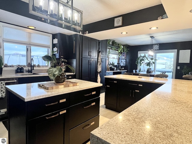 kitchen with light stone countertops, sink, decorative light fixtures, dishwasher, and a center island