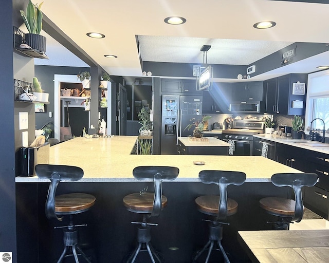 kitchen featuring a breakfast bar, a center island, sink, decorative light fixtures, and stainless steel appliances